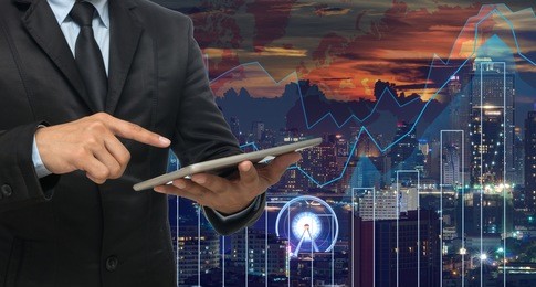 businessman using the tablet on trading graph on the cityscape at night and world map background,business financial concept