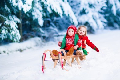 little girl and boy enjoy a sleigh ride. child sledding. toddler kid riding a sledge. children play outdoors in snow. kids sled in alps mountains in winter. outdoor fun for family christmas vacation.
