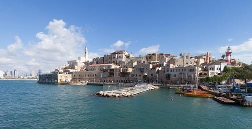 view of the old port of jaffa with a yacht passing by and the city of tel aviv in the background