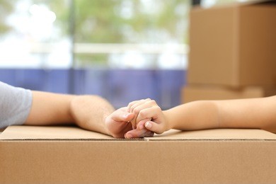 close up of a couple holding hands over a carton box and moving home