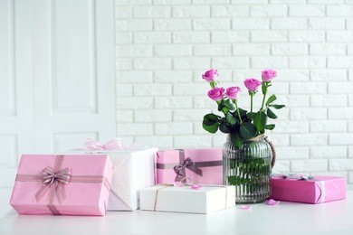 composition of colourful gift boxes and flowers in glass on white table in front of brick wall background