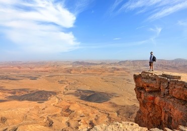 panoramic view of color stone desert of negev and traveler on the mountain top. national geological park hamakhtesh hagadol - large crater - a geological erosion land form, israel