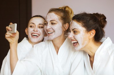 three young happy women with face masks taking selfi at spa resort. frenship and wellbeing concept