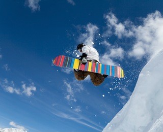 jumping snowboarder keeps one hand on the snowboard on blue sky background