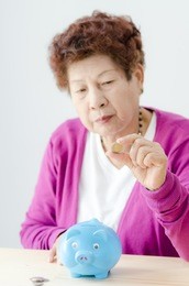 savings, money, annuity insurance, retirement and people concept - smiling senior woman putting coins into piggy bank at home