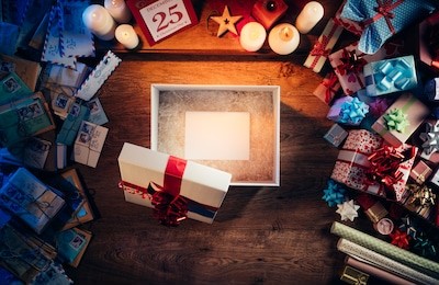 open gift box with a blank white card inside, presents and christmas letters all around, desktop top view