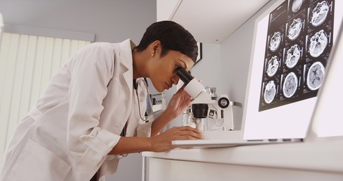 young intelligent  female doctor looking in a microscope