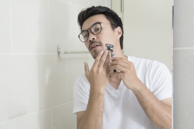reflection of a asian young man shaving in bathroom mirror