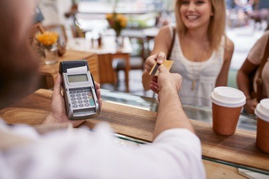 customer paying for their order with a credit card in a cafe. bartender holding a credit card reader machine and returning the debit card to female customer after payments.