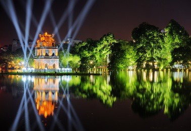 night view of the hoan kiem lake (lake of the returned sword) and the turtle tower among blue light rays at historic centre of hanoi in vietnam. the tower reflected in the lake.