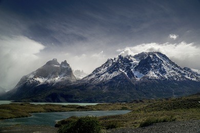 capped mountain chains with snow, with a foreground of green lakes, under a sky that becomes cloudy.