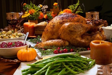 roasted turkey garnished with cranberries on a rustic style table decoraded with pumpkins, gourds, asparagus, brussel sprouts, baked vegetables, pie, flowers, and candles.
