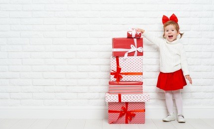 happy little girl child with christmas gifts at a blank brick wall