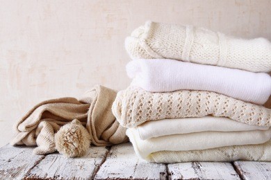 stack of white cozy knitted sweaters on a wooden table
