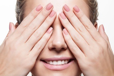 woman with beautiful natural manicure closes eyes with her hands
