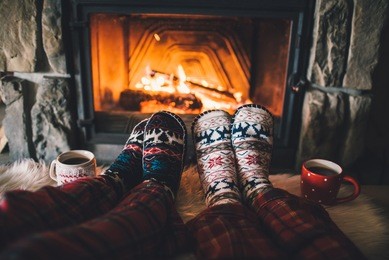 feet in woollen socks by the christmas fireplace. couple sitting under the blanket, relaxes by warm fire and warming up their feet in woollen socks. winter and christmas holidays concept.