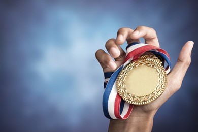 hand holding up a gold trophy cup/ medal as a winner in a competition