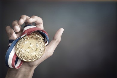 hand holding up a gold trophy cup/ medal as a winner in a competition
