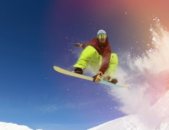 jumping snowboarder keeps one hand on snowboard in mountains in ski resort on blue sky background