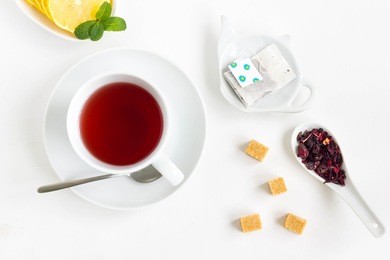 tea set with a cup of fruit tea, lemon, filter in teapot-shaped bowl, cube sugar and tea flowers. white background, top view, minimal style.