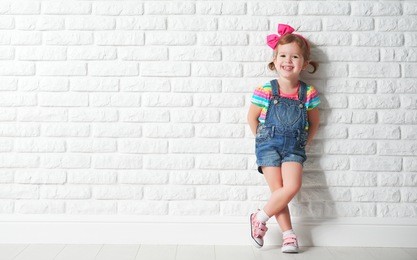 happy child little girl laughing at a blank empty brick wall
