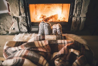 feet in woollen socks by the christmas fireplace. couple sitting under the blanket, relaxes by warm fire and warming up their feet in woollen socks. winter and christmas holidays concept.