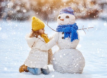 happy child girl plaing with a snowman on a snowy winter walk