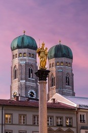 mary's column at marienplatz with out-of-focus towers of frauenkirche (cathedral of our dear lady) in the background at sunset, munich, bavaria, germany