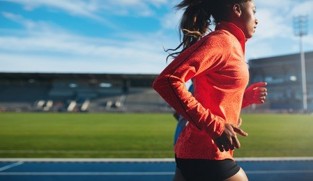 side view of fit young woman running. african female athlete training on race track at athletics stadium.