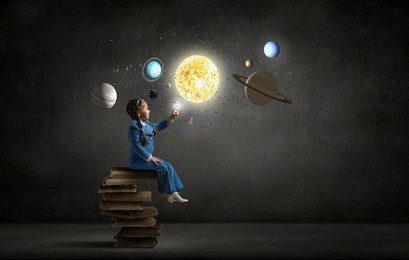 little girl sitting on stack of books and touching planet