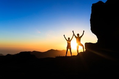 teamwork couple hikers success in sunset mountains, accomplish with arms up outstretched. young man and woman on rocky mountain range looking at beautiful inspirational landscape view, gran canaria.
