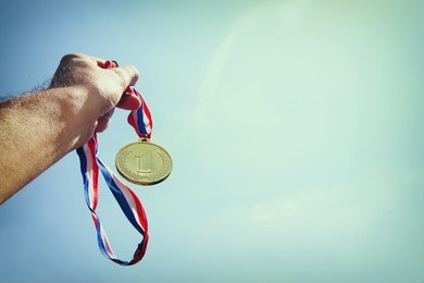man hand raised, holding gold medal against sky. award and victory concept. selective focus. retro style image.

