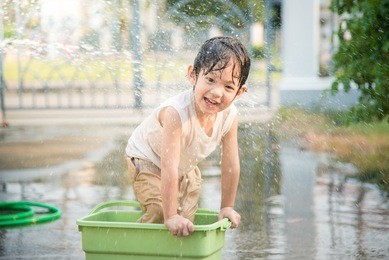 cute asian boy has fun playing in water from a hose