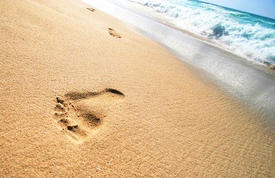 foot prints on tropical sandy beach and sea waves in the background