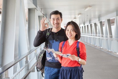  asian traveling man and woman standing with toothy smiling face with guide book in hand