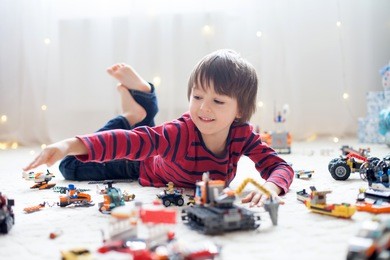 little child playing with lots of colorful plastic toys indoor, building different cars and objects
