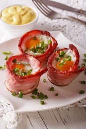 fried eggs wrapped in crispy bacon on a plate and sauce on the table. vertical