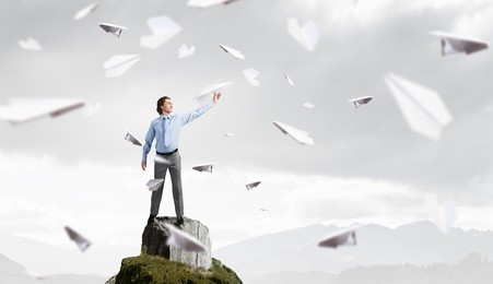 young businessman on rock top with paper plane in hand