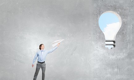 young businessman in concrete room with paper plane in hand