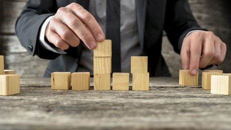concept of business strategy and planning - front view of male hand placing and positioning wooden blocks in various structures.