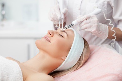 close up of hands of professional beautician touching female forehead with the equipment. the young woman is lying and smiling