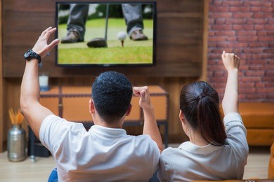asian couple having fun watching golf game in living room
