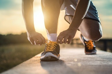 man tying jogging shoes.a person running outdoors on a sunny day.focus on a side view of two human hands reaching down to a athletic shoe.