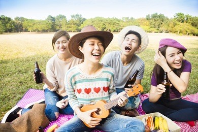 happy young friends enjoying picnic and playing ukulele 