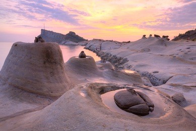 beautiful reflections of rosy sunrise sky at yehliu coastal geologic park with unique candlestick rock formations along rocky coast under dramatic dawning sky in northern taiwan (long exposure effect)