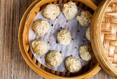 high angled view of cooked dumplings inside of bamboo steamer with lip partially off. 