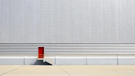 the sheet metal factory wall with the red  entrance door in the industrial park.the red door of the factory building.