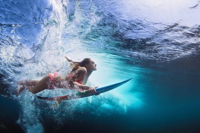 young girl in bikini - surfer with surf board dive underwater with fun under big ocean wave. family lifestyle, people water sport lessons and beach swimming activity on summer vacation with child