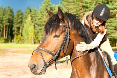 girl equestrian riding horseback and stroking horse neck. vibrant summertime horizontal outdoors image.