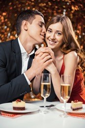 romantic photo of beautiful couple on glitter gold background. couple having date at valentine's day. lovers having dinner. there are glasses with champagne and desserts on table
